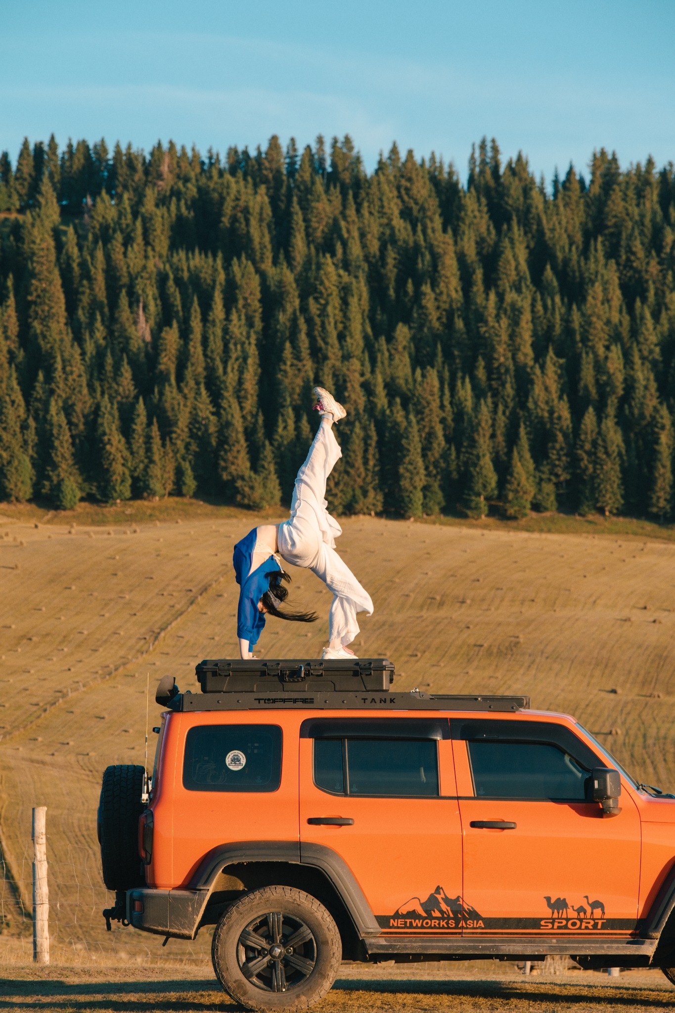 Anna practicing a handstand on an orange vehicle in a forest landscape